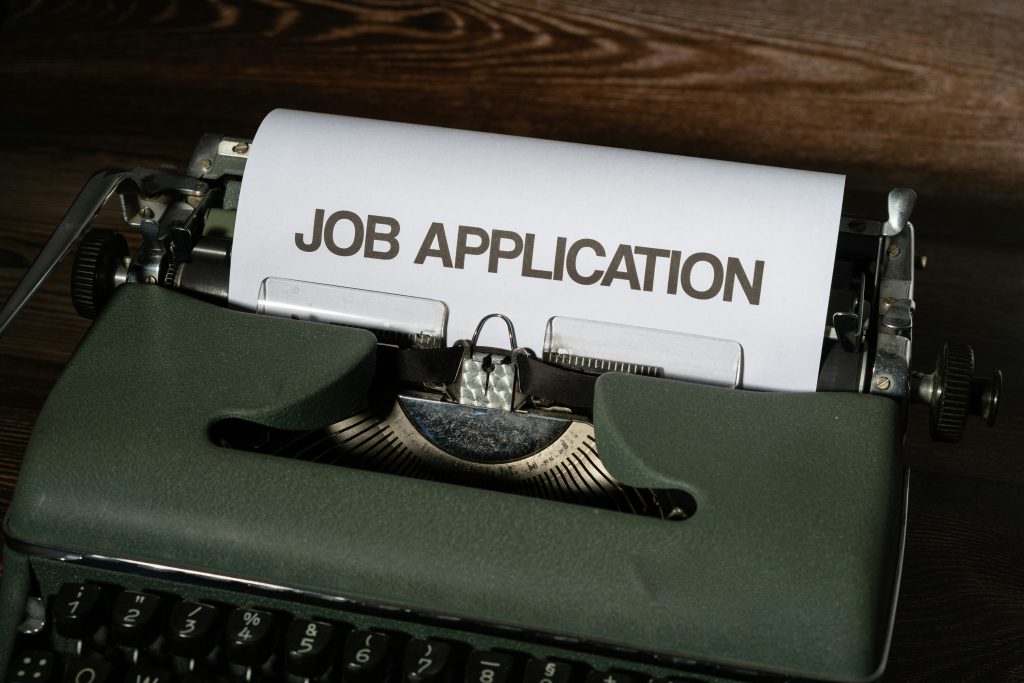 Job application is written on a piece of white paper that's emerging from a type writer.