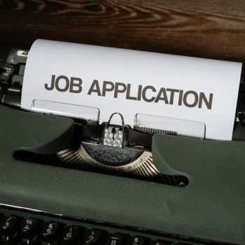 Job application is written on a piece of white paper that's emerging from a type writer.